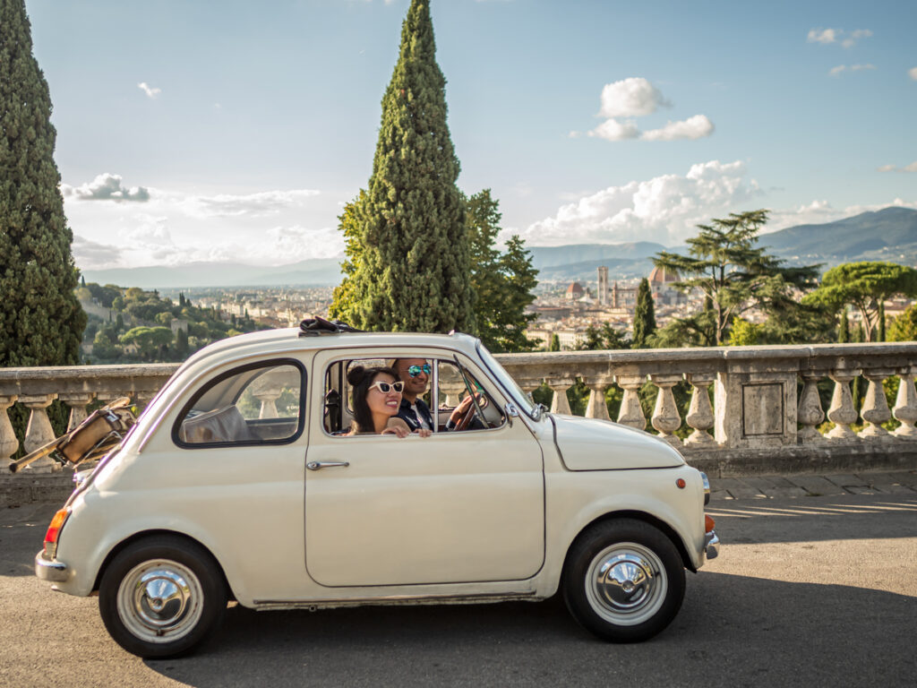 A couple in a vintage car driving in Florence Italy. The streets look empty as they cover the best day of the week to visit Florence. 