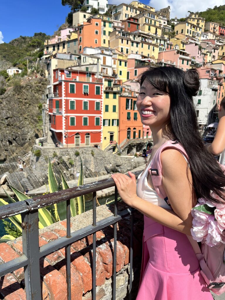 Jade posing in front of the enchanting cityscape of Riomaggiore, one of the stunning villages in Cinque Terre, Italy.