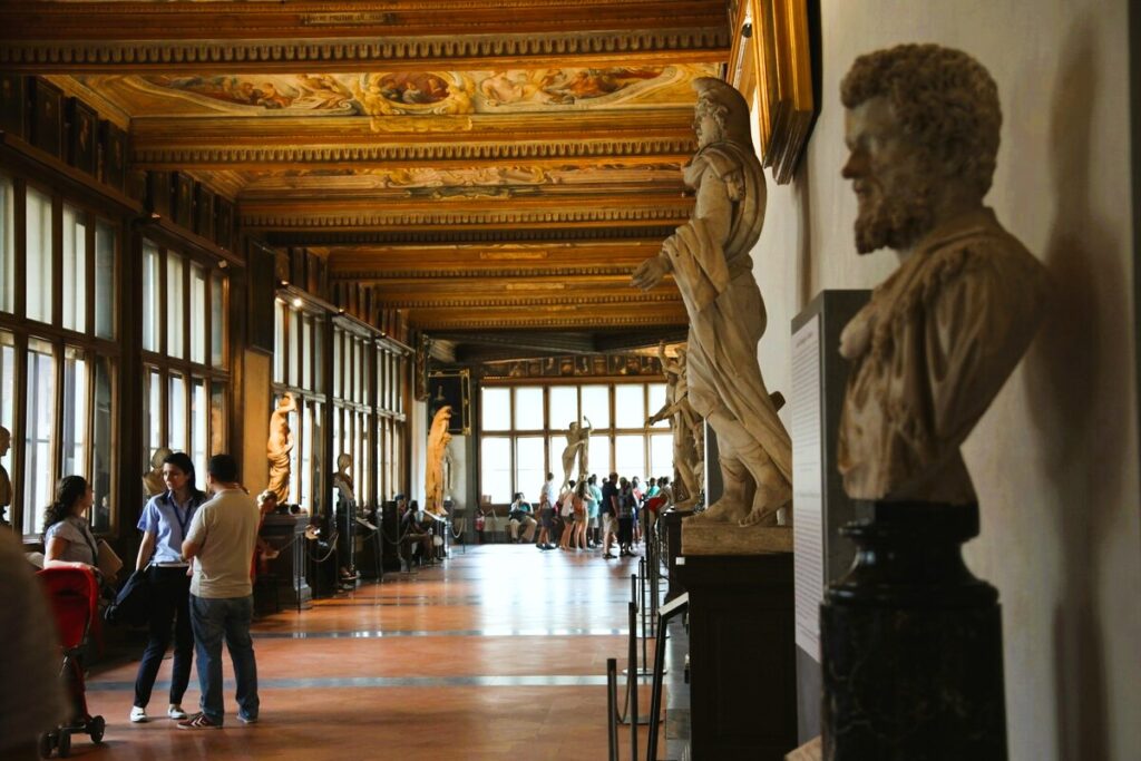 Grandeous room in Uffizi Gallery with people meeting Uffizi Gallery dress code, and sculptures and paintings. Piazzale degli Uffizi is in Florence Italy